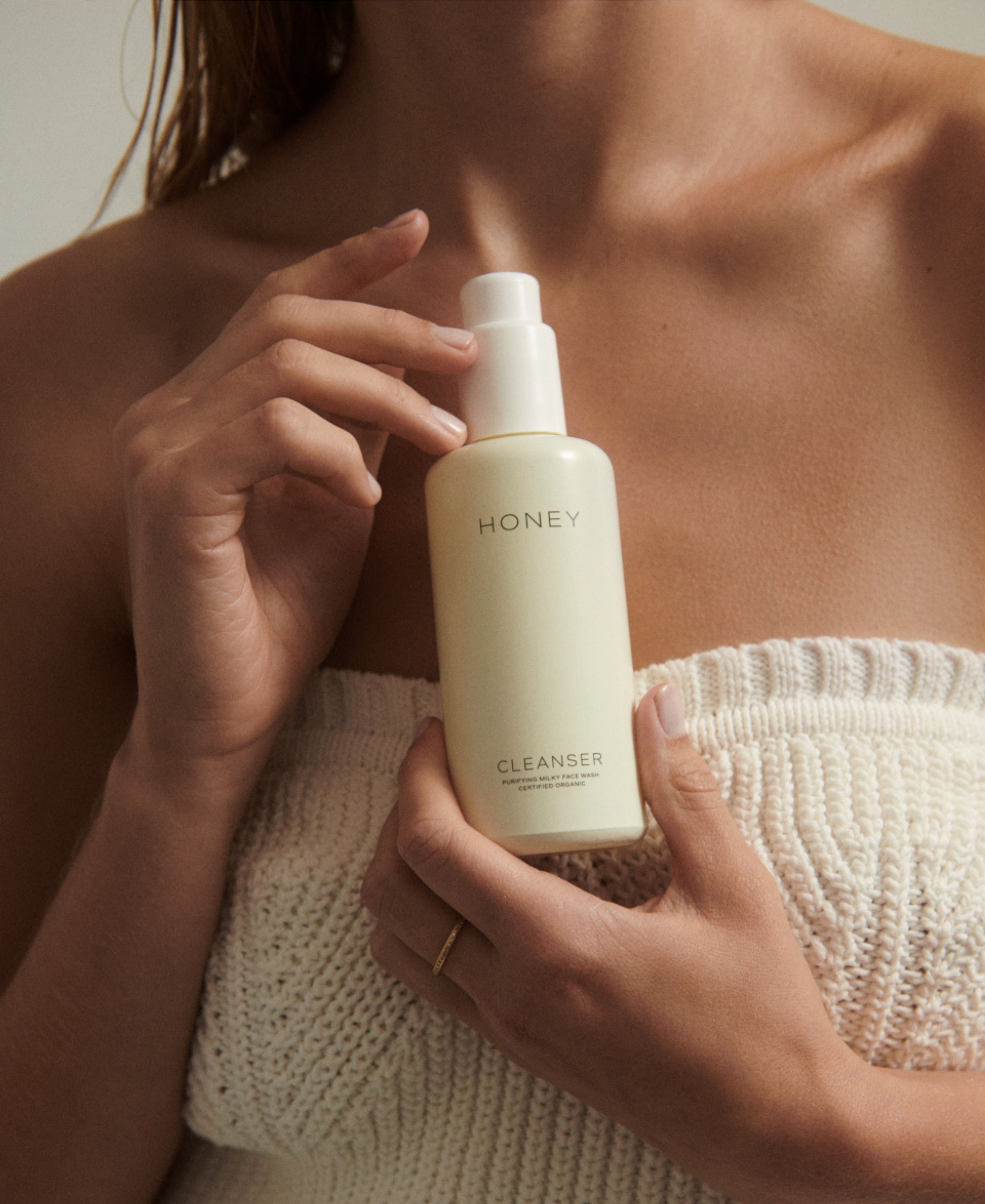 Woman in white top holding natural fragrance-free cleanser - face wash in light yellow bottle with white cap