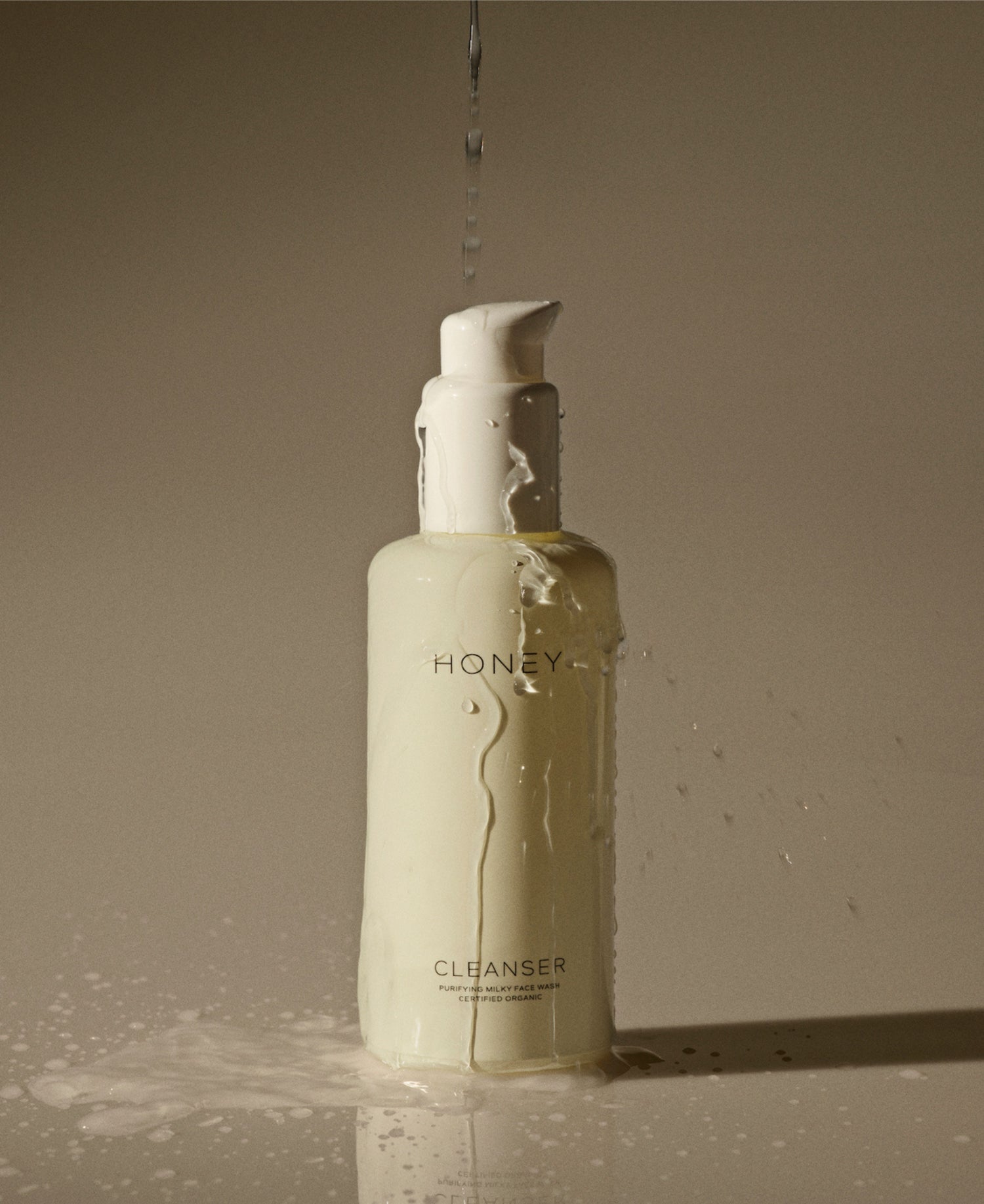 Natural clean skincare cleanser - face wash in light yellow bottle with white cap with water pouring over it