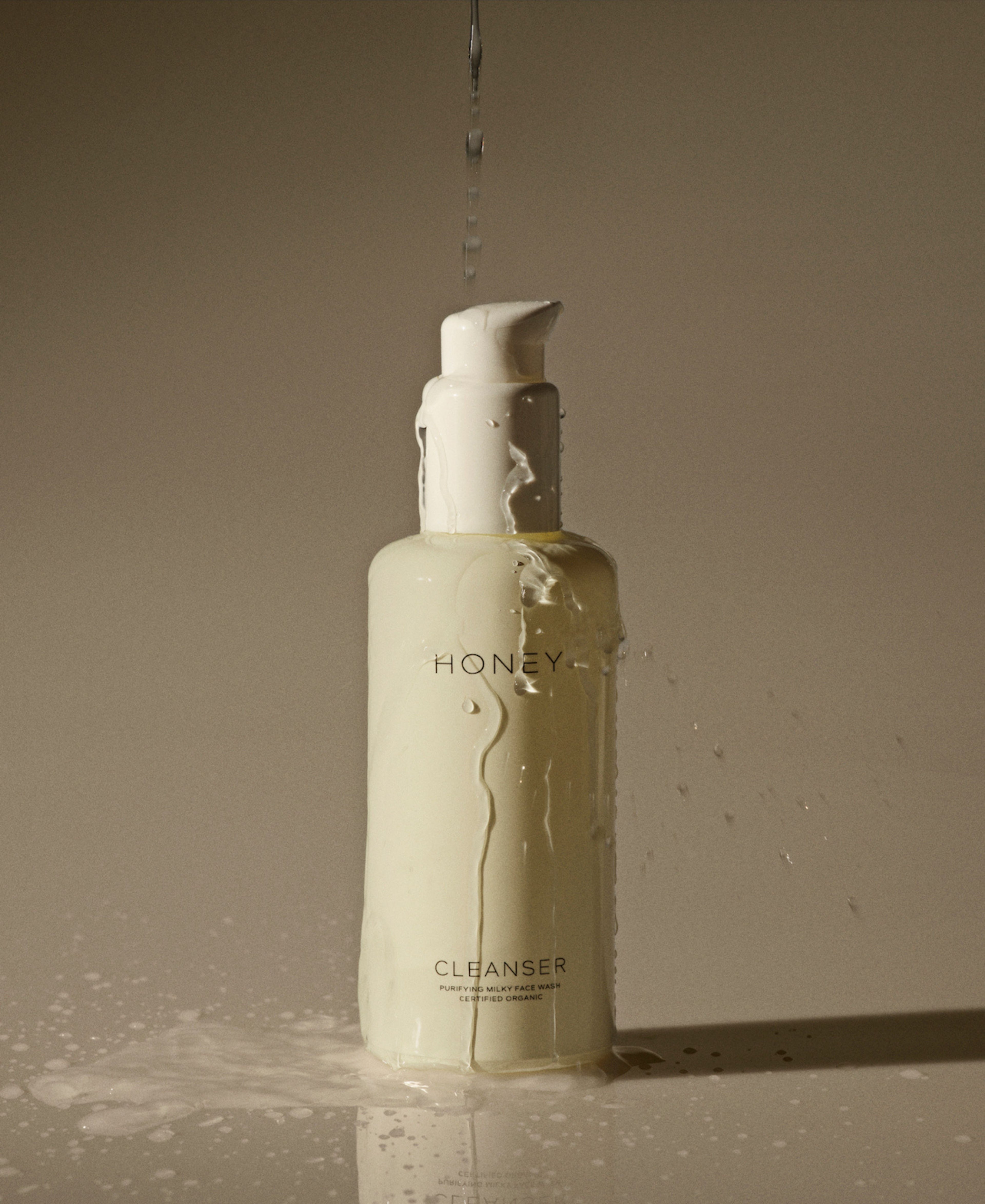Natural clean skincare cleanser - face wash in light yellow bottle with white cap with water pouring over it