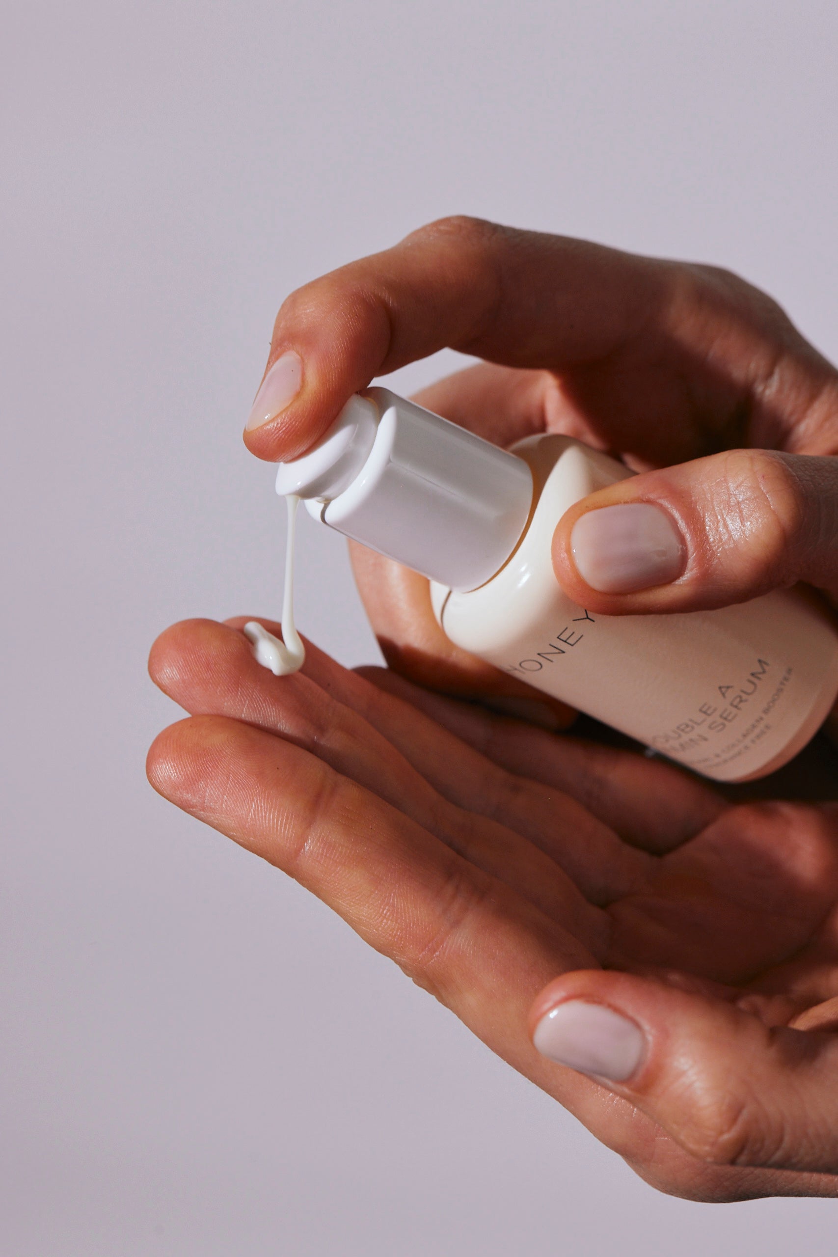 Hand pouring double A vitamin serum from light pink bottle with white cap - natural and clean skincare