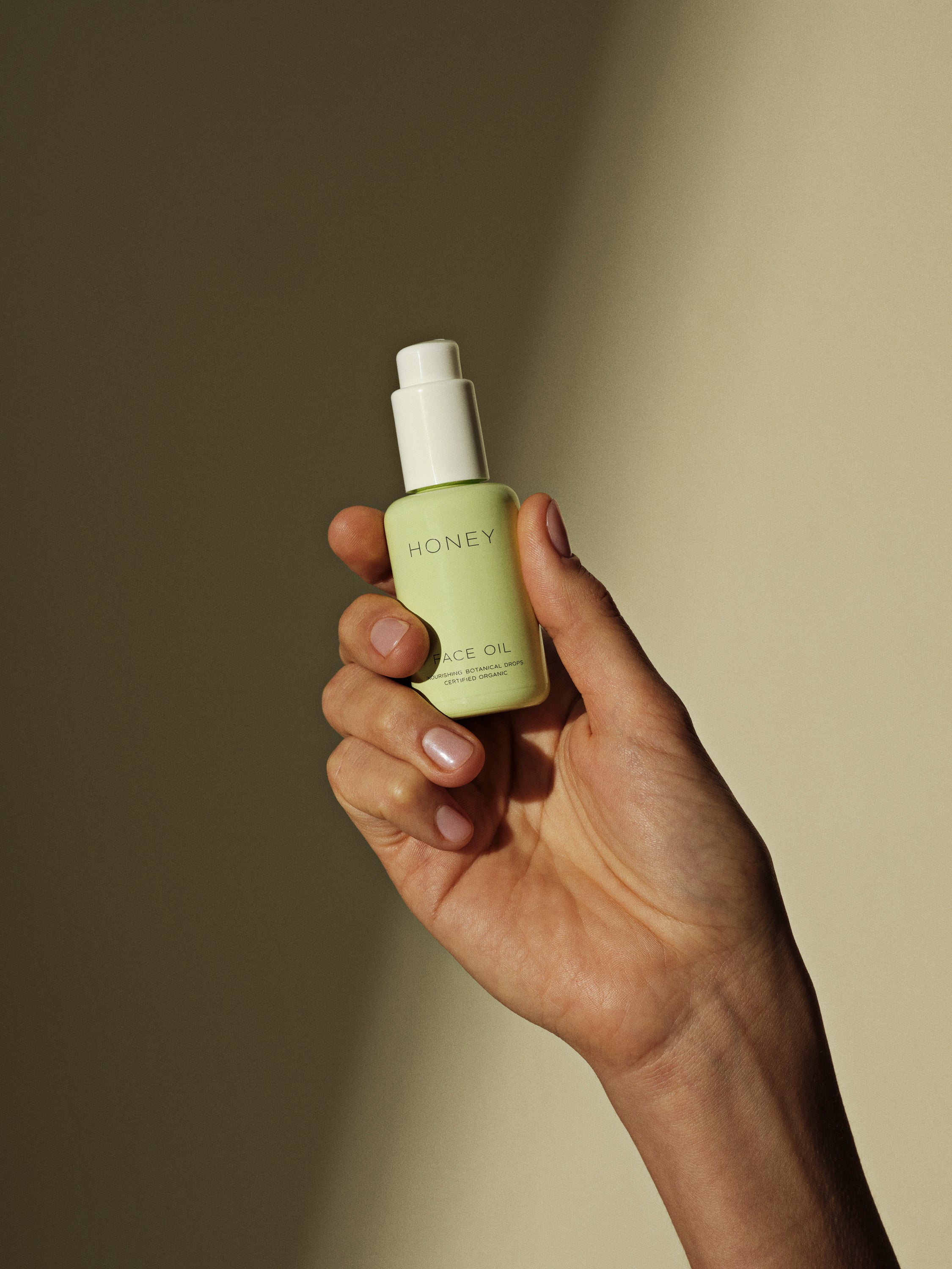 Hand holding natural face oil in green bottle with white cap - clean skincare
