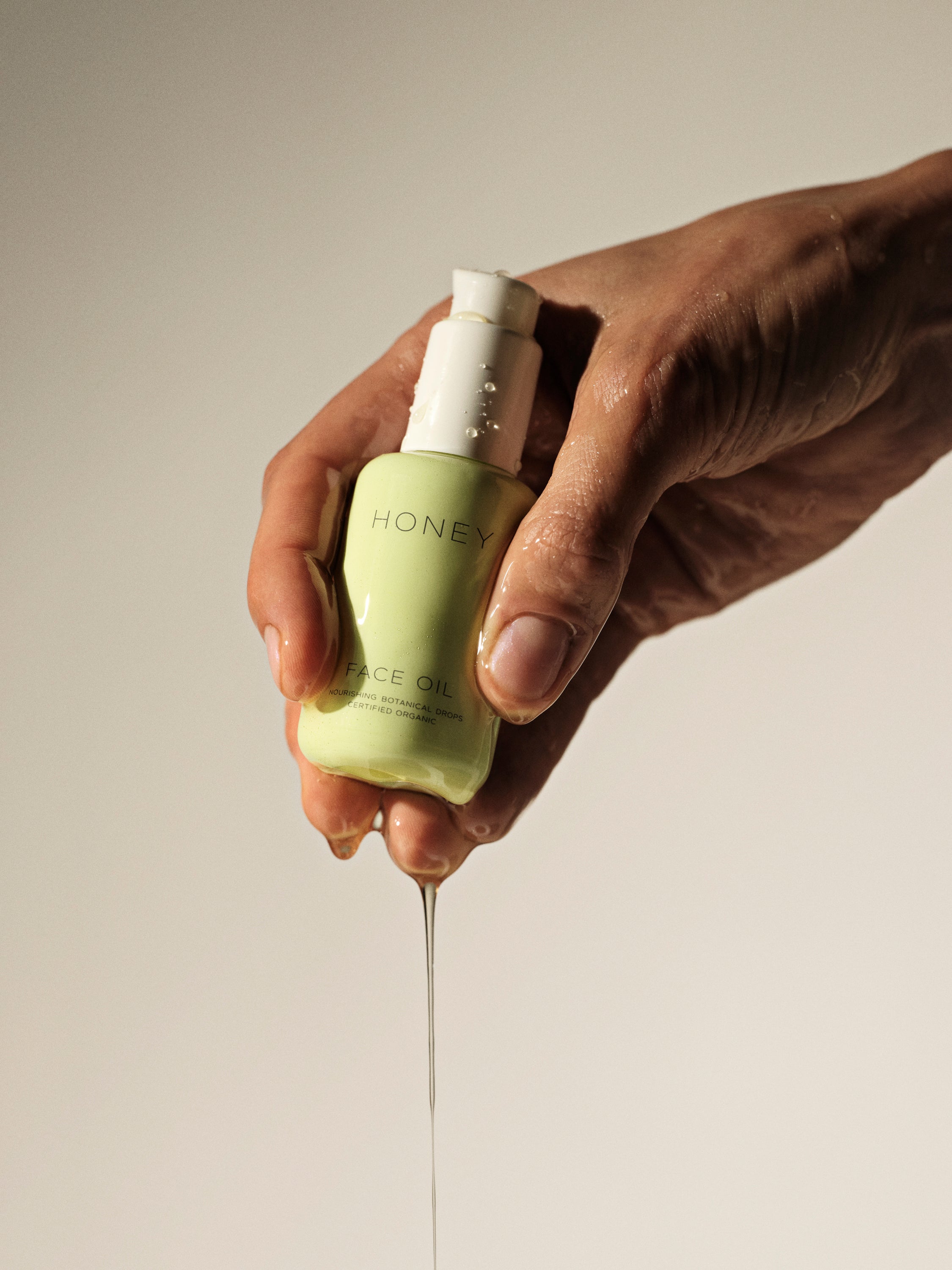 Hand holding natural face oil in green bottle with white cap - clean skincare