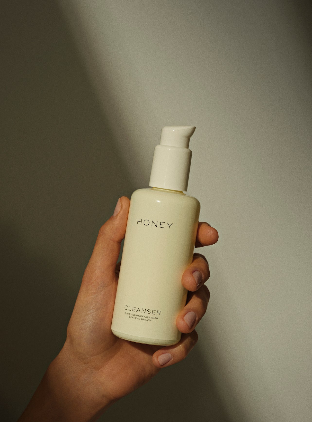 Hand holding natural fragrance-free cleanser - face wash in light yellow bottle with white cap