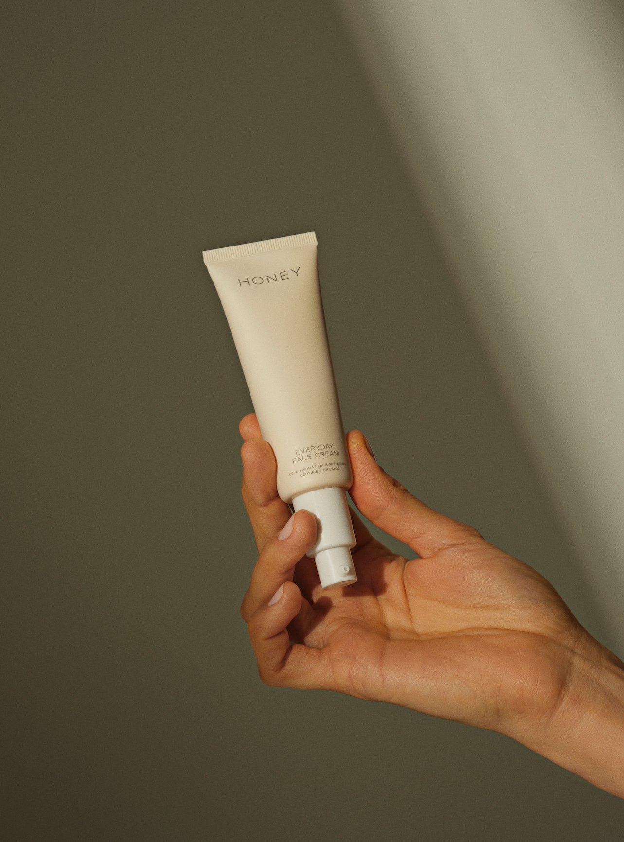 Hand holding fragrance-free face cream in light pink tube with white cap e