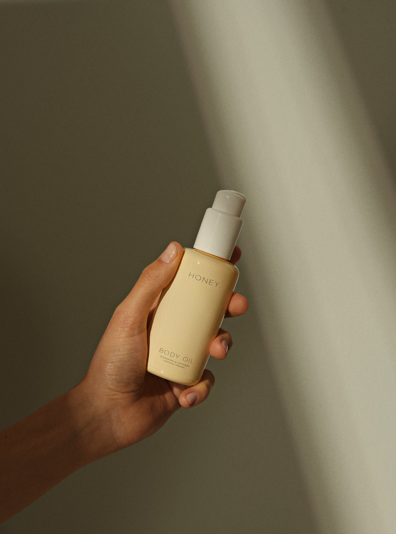 Hand holding yellow bottle with white cap containing clean skincare natural body oil