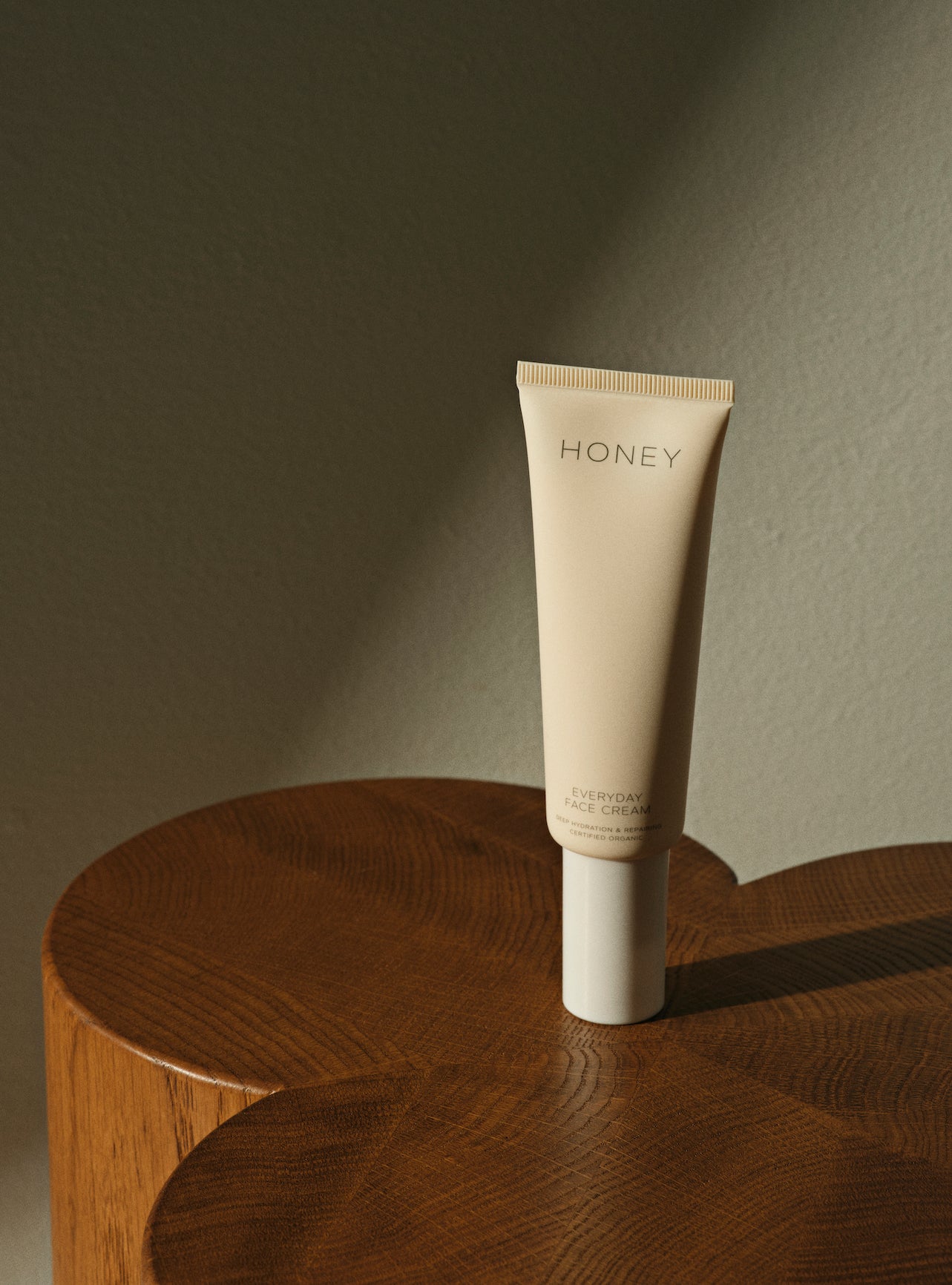 Natural fragrance-free day face cream in light pink tube with white cap standing on wooden table