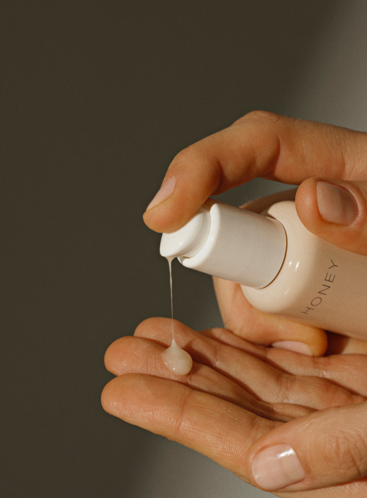 Hand pouring natural hydra serum from dusty pink bottle with white cap - fragrance-free clean skincare